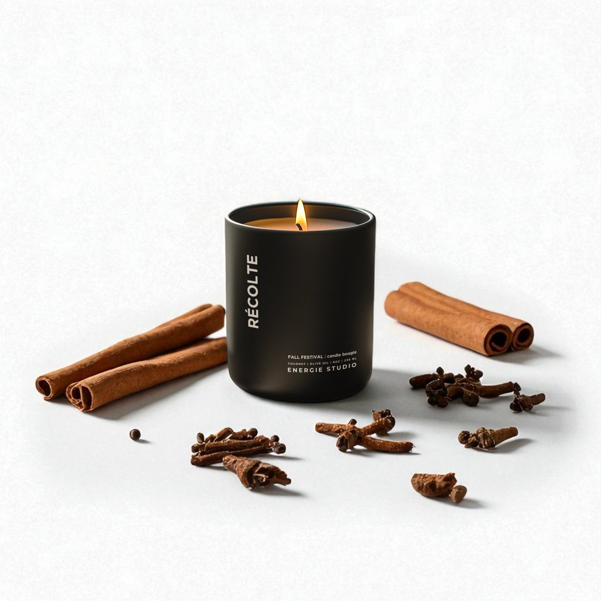 Black candle labeled 'Reçolte' with cinnamon sticks and cloves on a white background