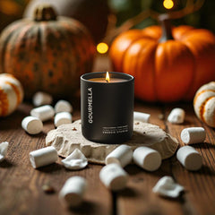 Gourmella candle on a wooden surface with pumpkins and marshmallows in the background