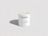 White candle with 'Pine Needles' label on a light gray background