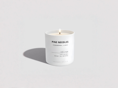White candle with 'Pine Needles' label on a light gray background