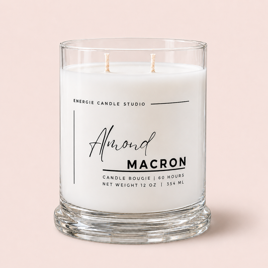 A two-wick scented candle in a clear glass jar with a thick base, featuring white wax and a printed label that reads 'Almond MACRON' and 'ENERGIE CANDLE STUDIO' on a soft pink background.