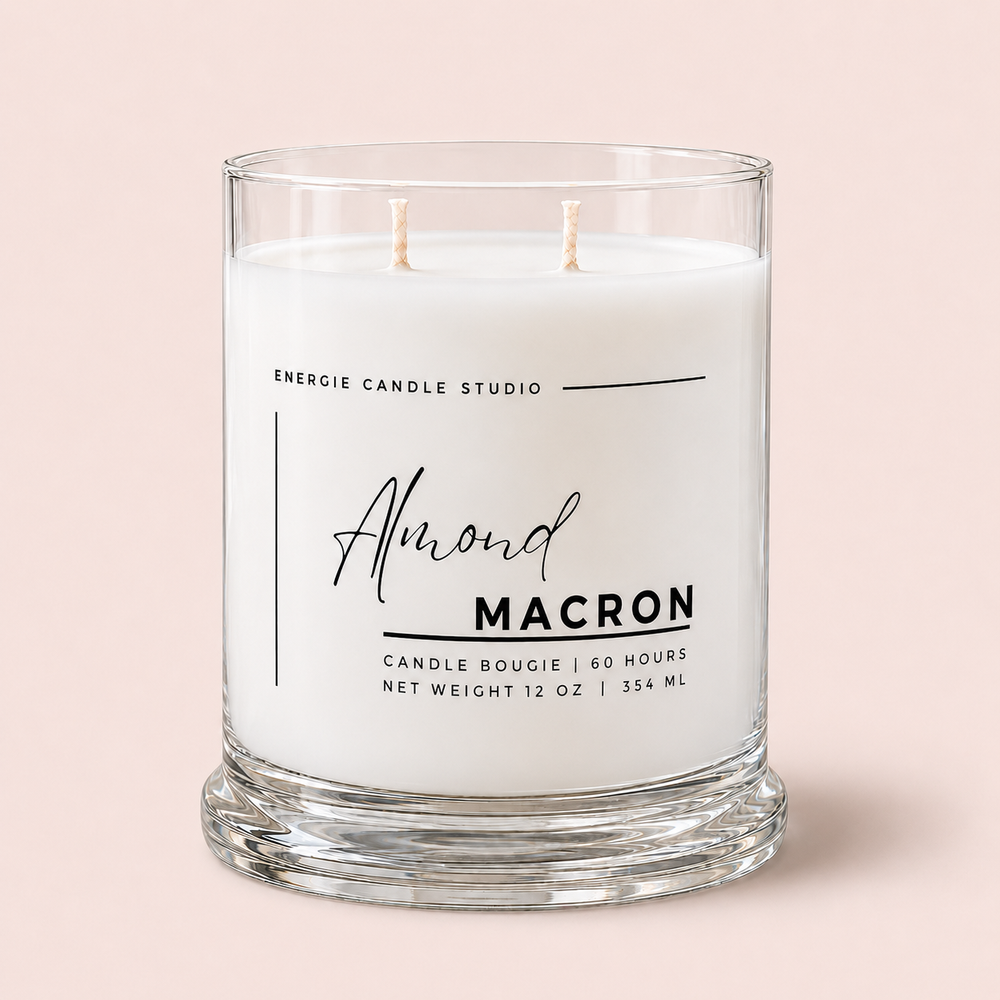 A two-wick scented candle in a clear glass jar with a thick base, featuring white wax and a printed label that reads 'Almond MACRON' and 'ENERGIE CANDLE STUDIO' on a soft pink background.