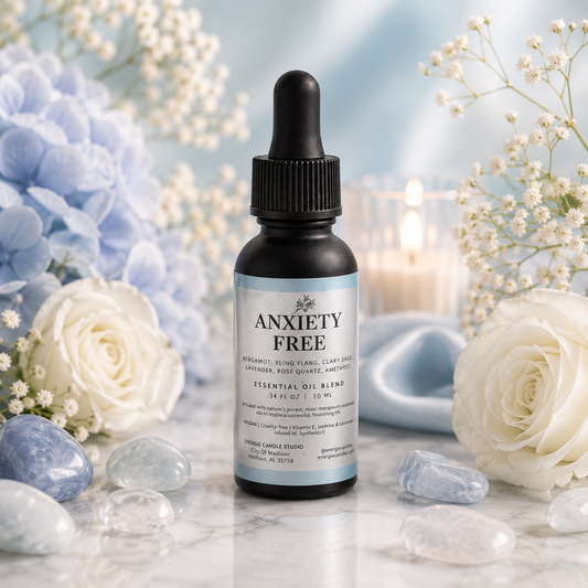A small amber dropper bottle labeled 'ANXIETY FREE' stands centered on a marble surface, surrounded by white and blue flowers, clear stones, and soft blue background decor.