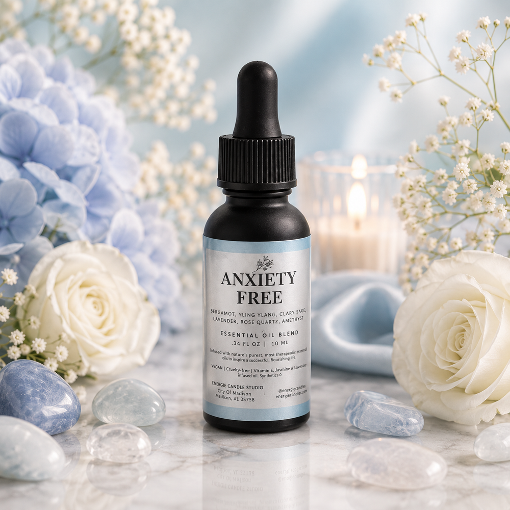 A small amber dropper bottle labeled 'ANXIETY FREE' stands centered on a marble surface, surrounded by white and blue flowers, clear stones, and soft blue background decor.