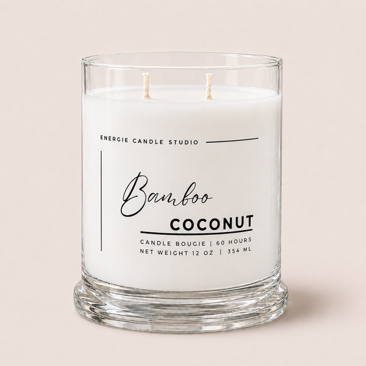 A two-wick scented candle in a clear glass jar with a thick base, labeled 'Bamboo COCONUT' by Energie Candle Studio, on a solid pale pink background.