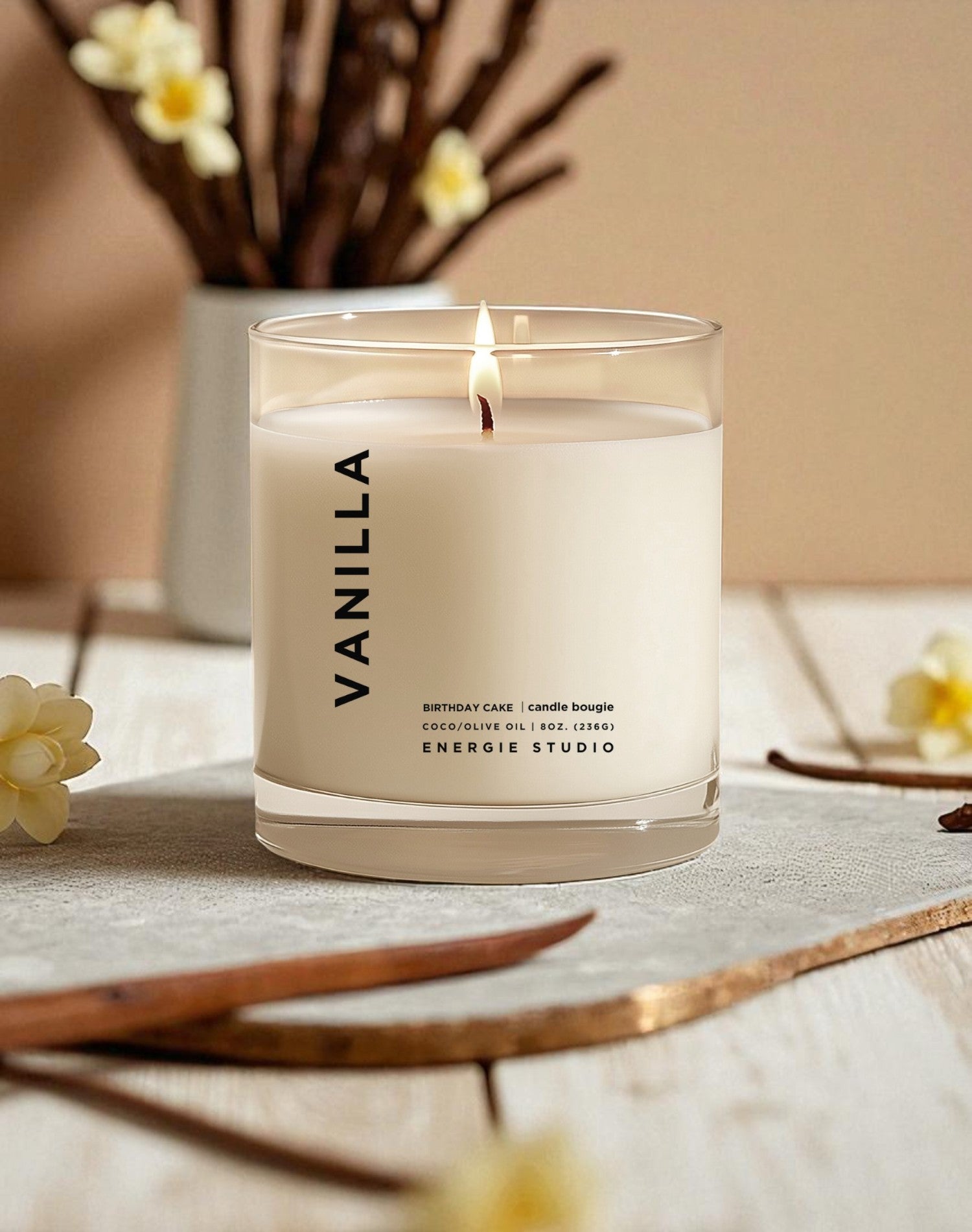 Vanilla candle in a glass jar on a table with flowers and a neutral background