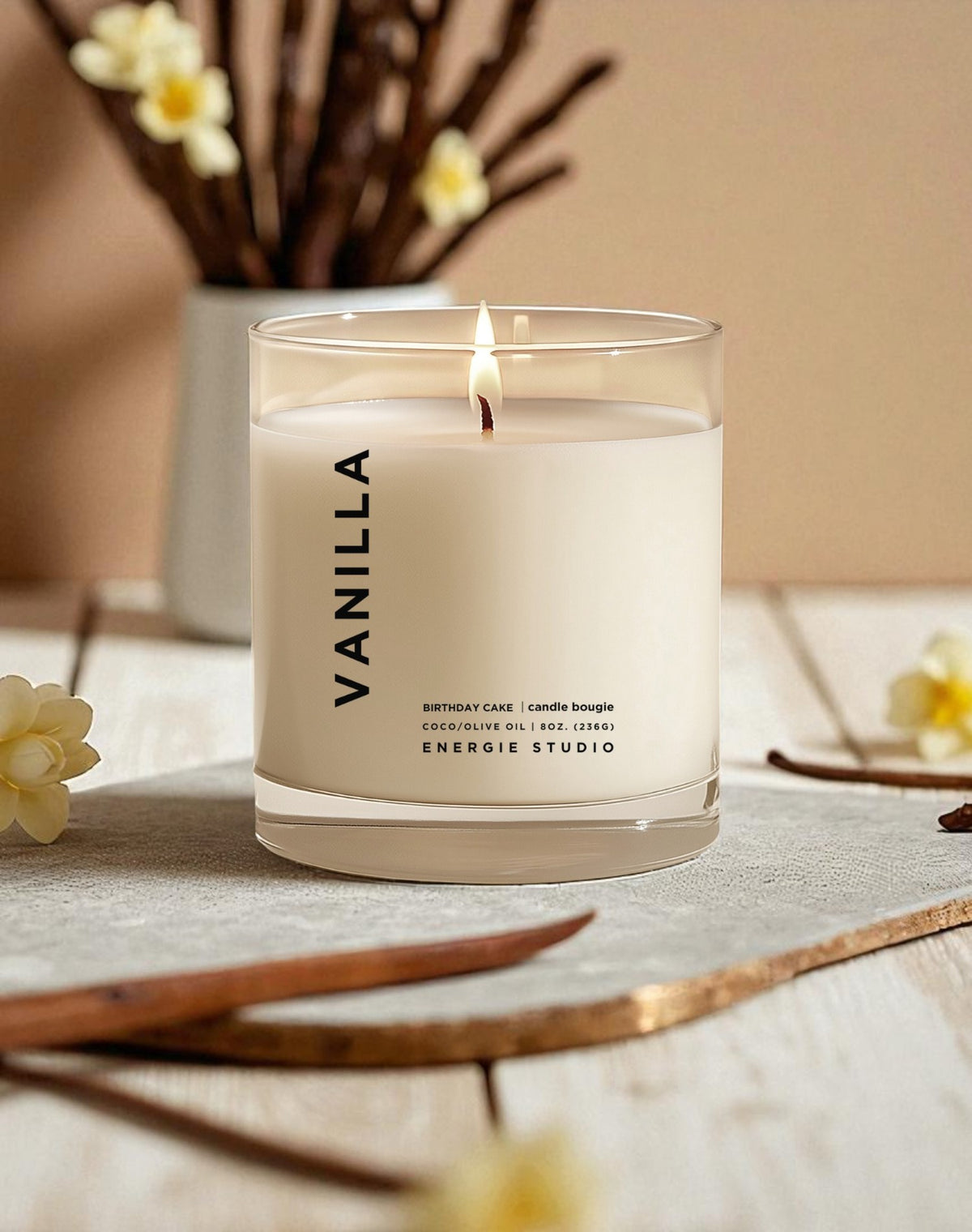 Vanilla candle in a glass jar on a table with flowers and a neutral background