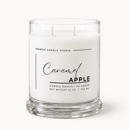 A two-wick candle in a clear glass jar with white wax, labeled 'Caramel Apple' by Energie Candle Studio, on a light cream background.
