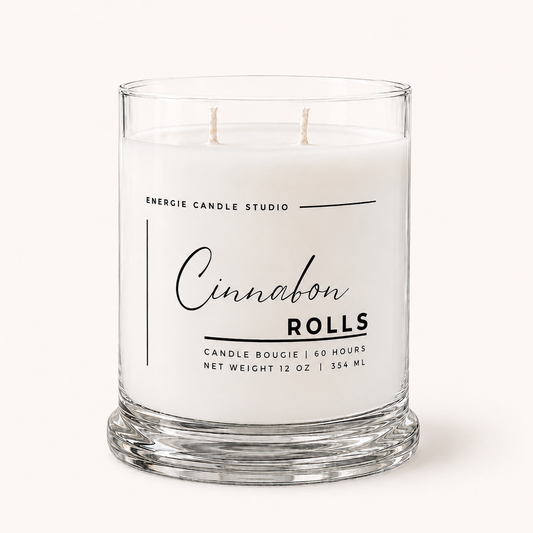 A two-wick scented candle in a clear glass jar with white wax, featuring a white label with black text that reads 'ENERGIE CANDLE STUDIO Cinnamon Rolls'.