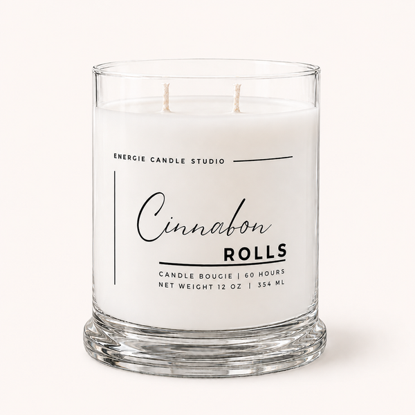 A two-wick scented candle in a clear glass jar with white wax, featuring a white label with black text that reads 'ENERGIE CANDLE STUDIO Cinnamon Rolls'.
