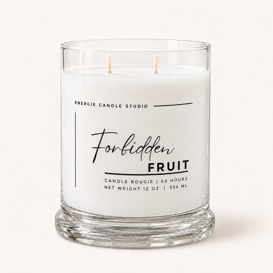 A two-wick glass jar candle with white wax and a clear glass base, featuring black text that reads 'Energie Candle Studio Forbidden Fruit' on the front, set against a solid off-white background.