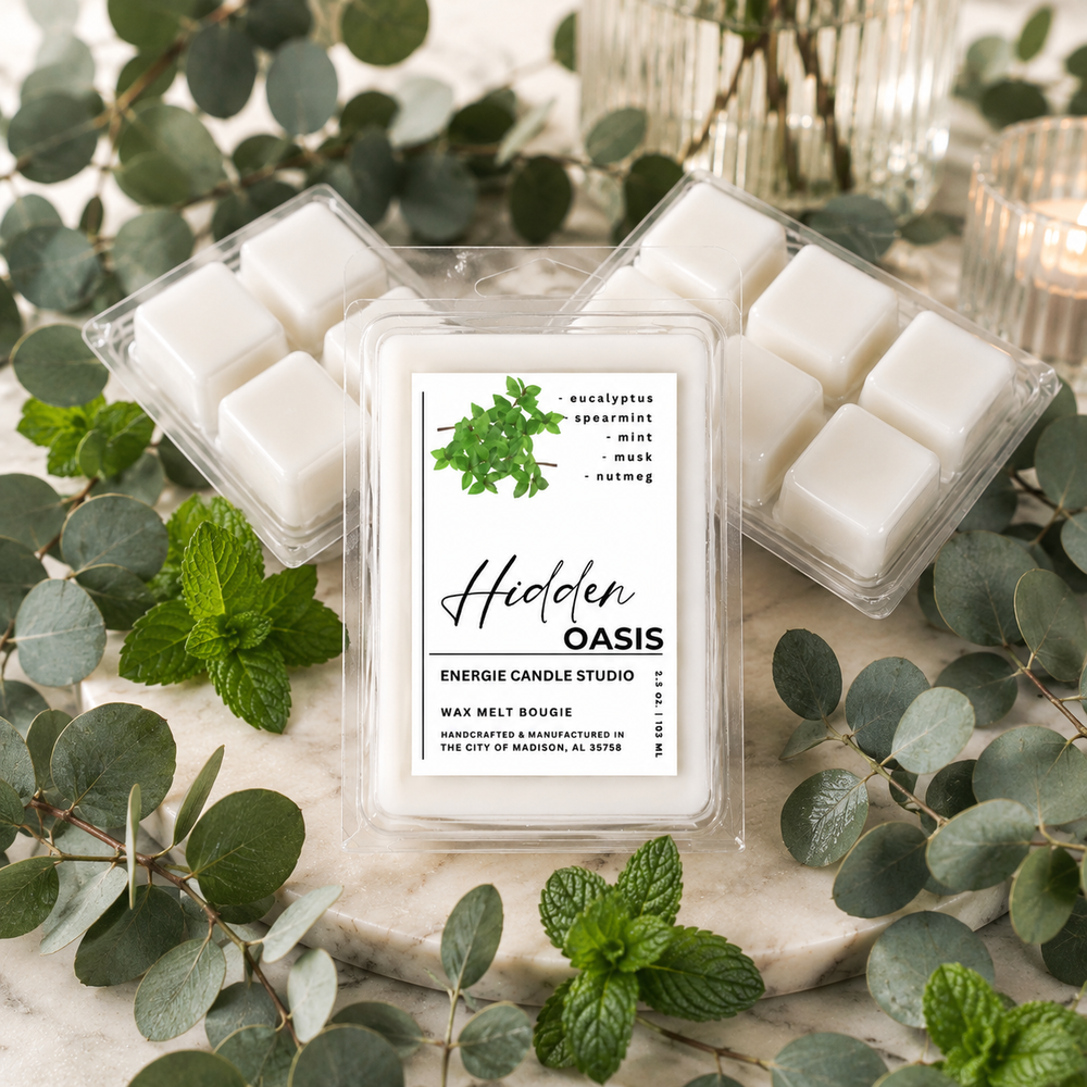 Three clear plastic clamshell wax melt containers arranged on a marble surface with eucalyptus leaves and mint. The center container is open and shows white wax cubes; the label reads 'Hidden Oasis' and 'Energize Candle Studio.