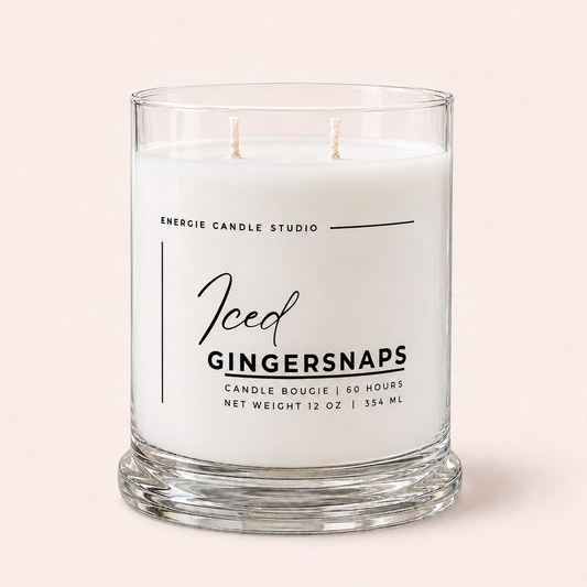 A two-wick scented candle in a clear glass jar with white wax, labeled 'Iced Gingersnaps' by Energie Candle Studio, set against a solid pale pink background.