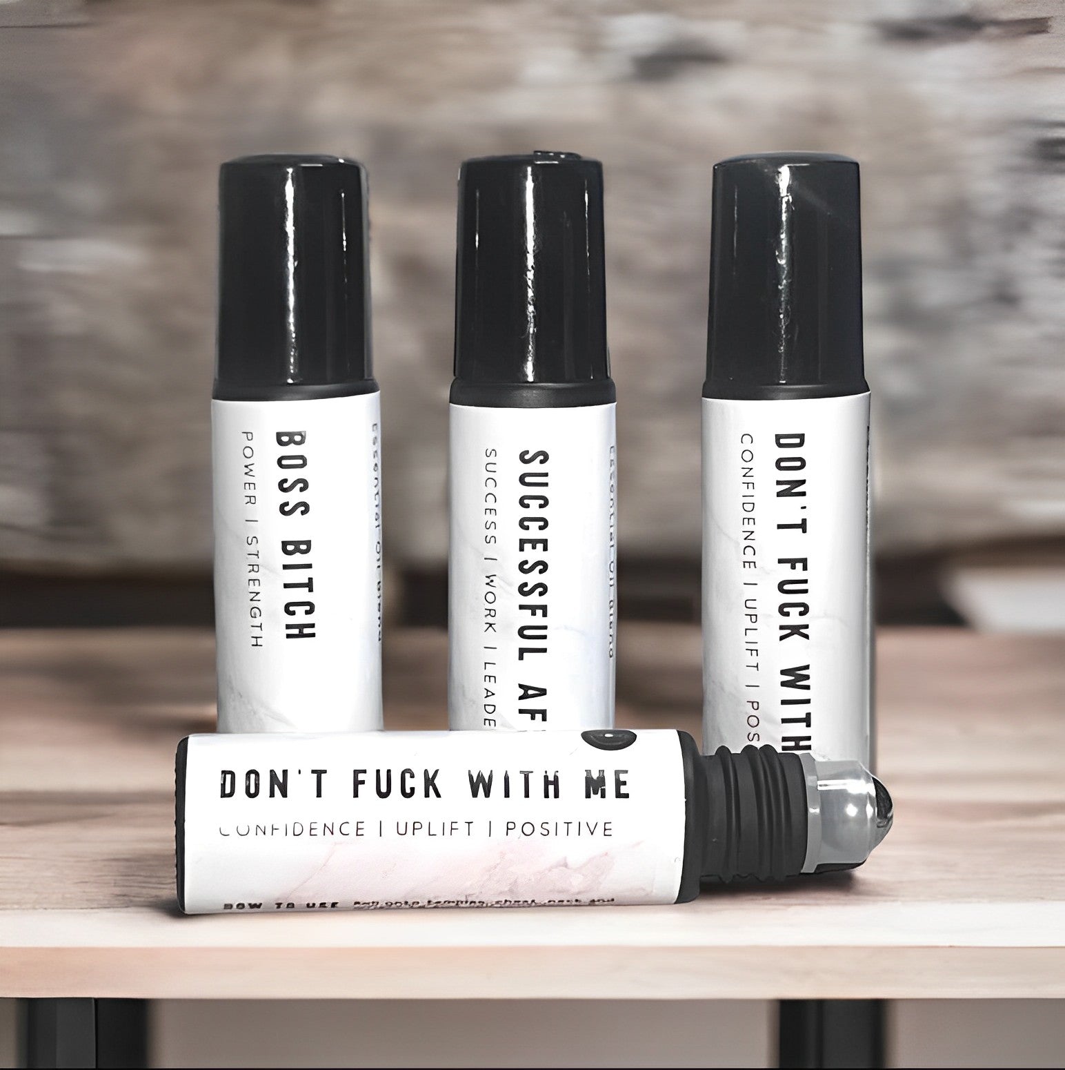 Four bottles of roll-on black oils with white labels, arranged on a wooden table with a blurred gray background.