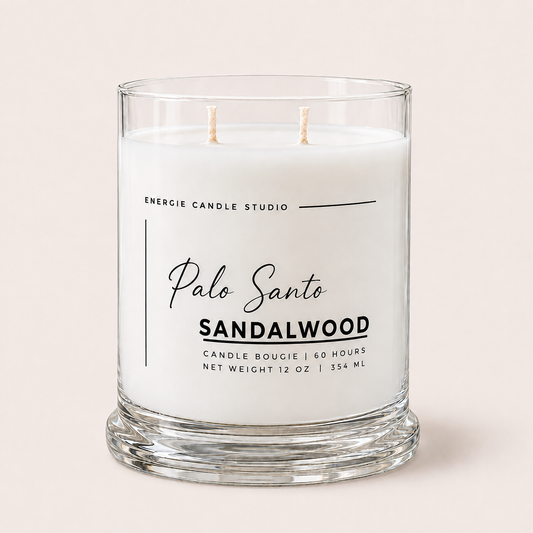 A two-wick candle in a clear glass jar with white wax, labeled 'Palo Santo SANDALWOOD' by Energie Candle Studio, set against a solid pale pink background.
