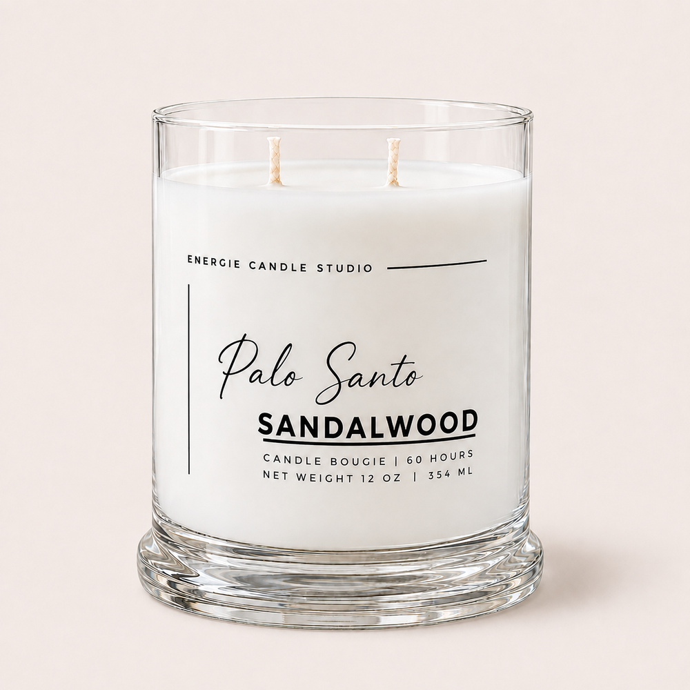 A two-wick candle in a clear glass jar with white wax, labeled 'Palo Santo SANDALWOOD' by Energie Candle Studio, set against a solid pale pink background.