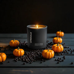 Peppered Pumpkin candle in a black vessel on a black wooden table surrounded by pepper and pumpkins