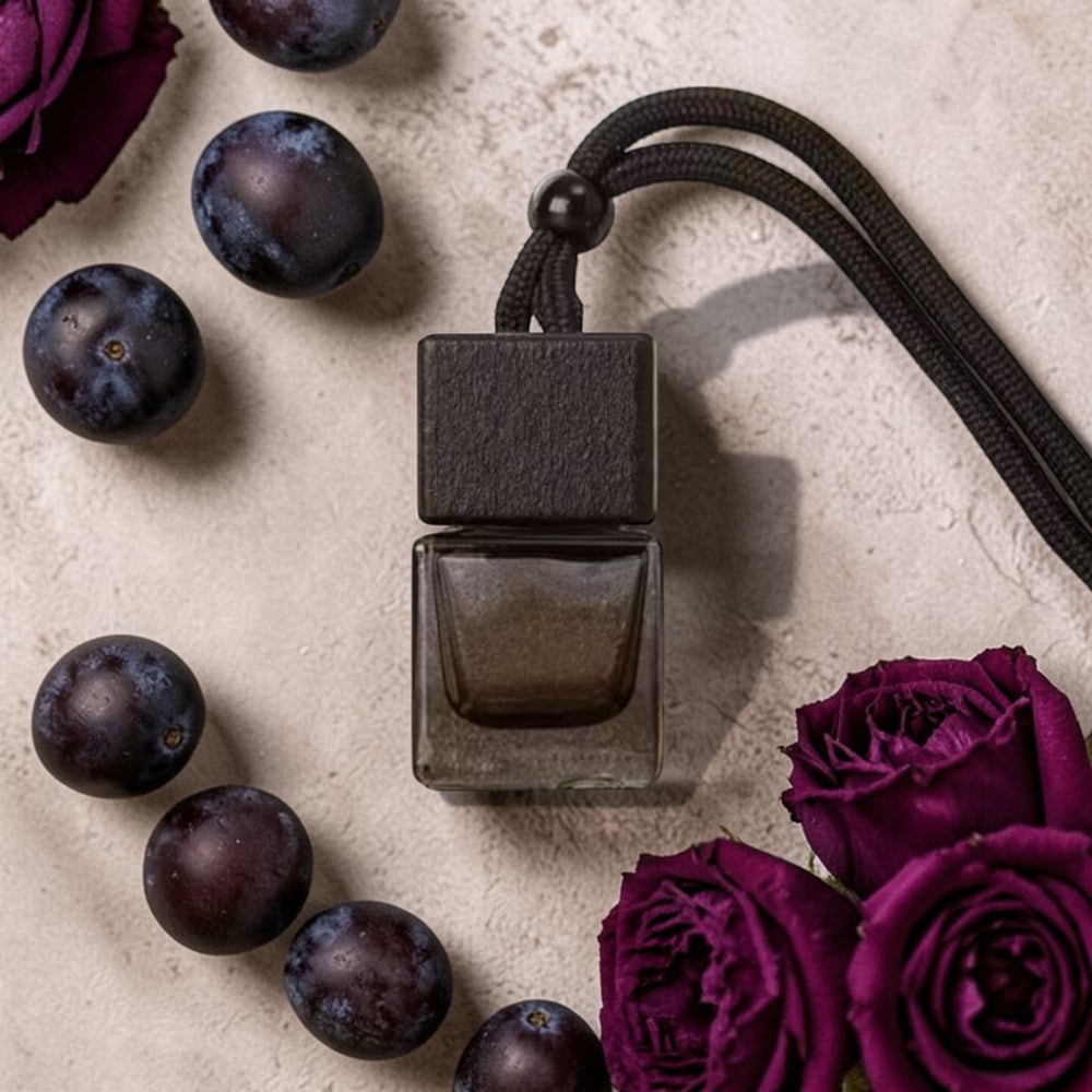Dark perfume bottle with purple flowers and plums on a textured surface