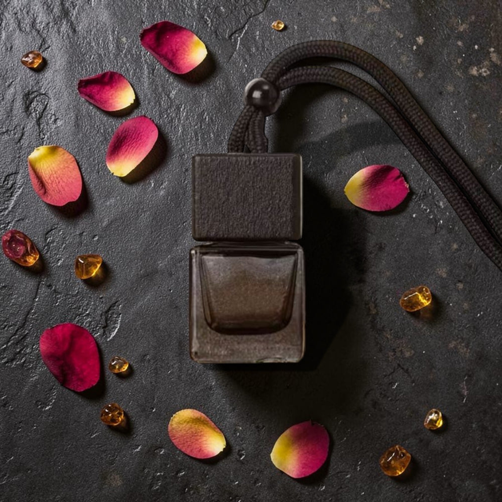 Dark brown perfume bottle with colorful petals and a rope on a dark surface
