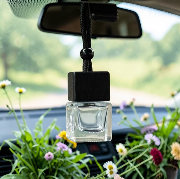 Car air freshener hanging from a car's rearview mirror with flowers and greenery in the background.