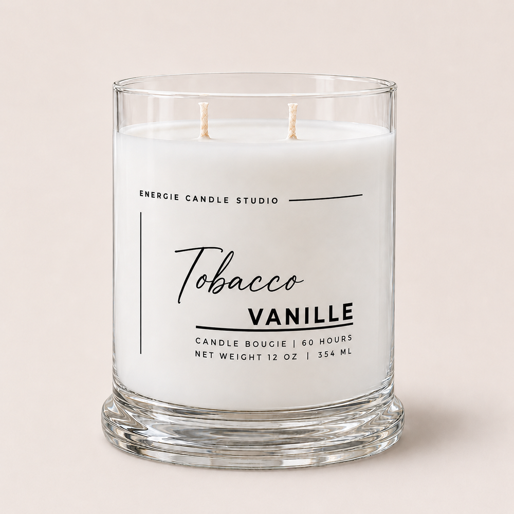 A two-wick scented candle in a clear glass jar with white wax, labeled 'Tobacco Vanille' by Energie Candle Studio, set against a solid light beige background.