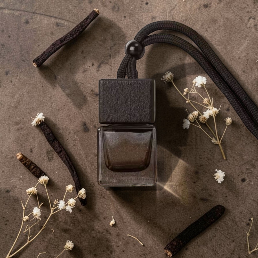Black perfume bottle with a rope on a textured surface with vanilla beans and flowers.
