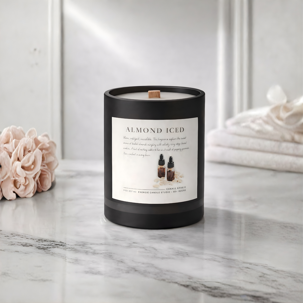 Candle labeled 'Almond Iced' on a marble surface with flowers and towels in the background
