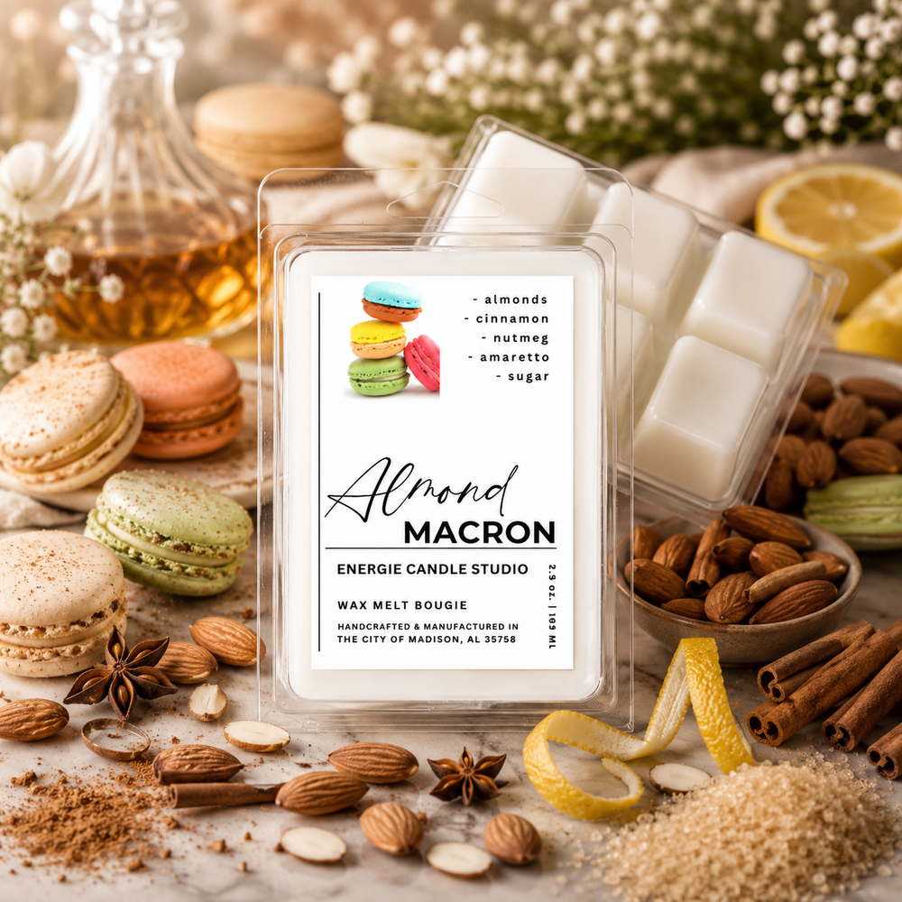 A clear clamshell package of Almond Macron scented wax melts sits on a marble surface surrounded by almonds, cinnamon sticks, macarons, star anise, sugar, lemon zest, and a glass bottle of oil. The front label reads 'Almond MACRON' and 'ENERGIE CANDLE STUDIO'.