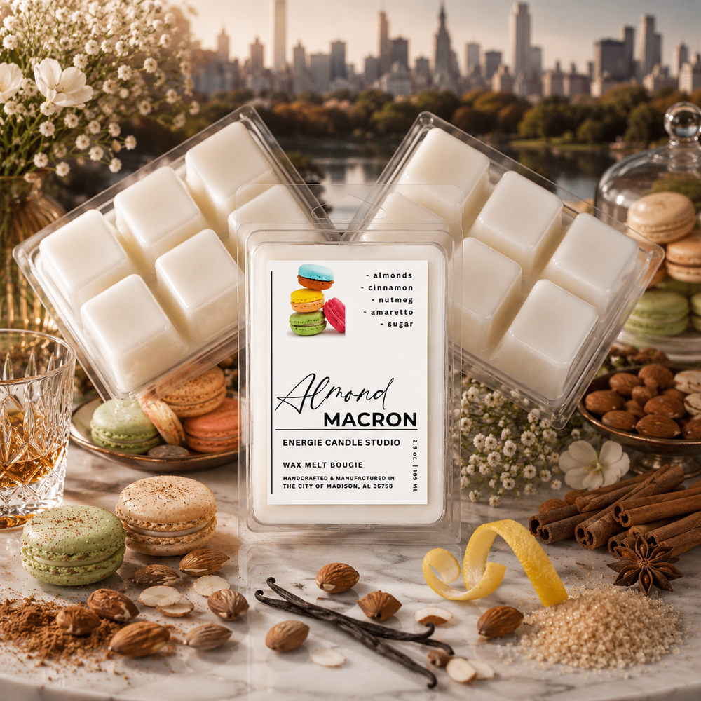 Three wax melts in clear plastic clamshell containers are arranged on a marble surface with macarons, nuts, cinnamon sticks, and a city skyline in the background. The center container has a white label reading 'Almond MACRON' and 'ENERGIE CANDLE STUDIO.