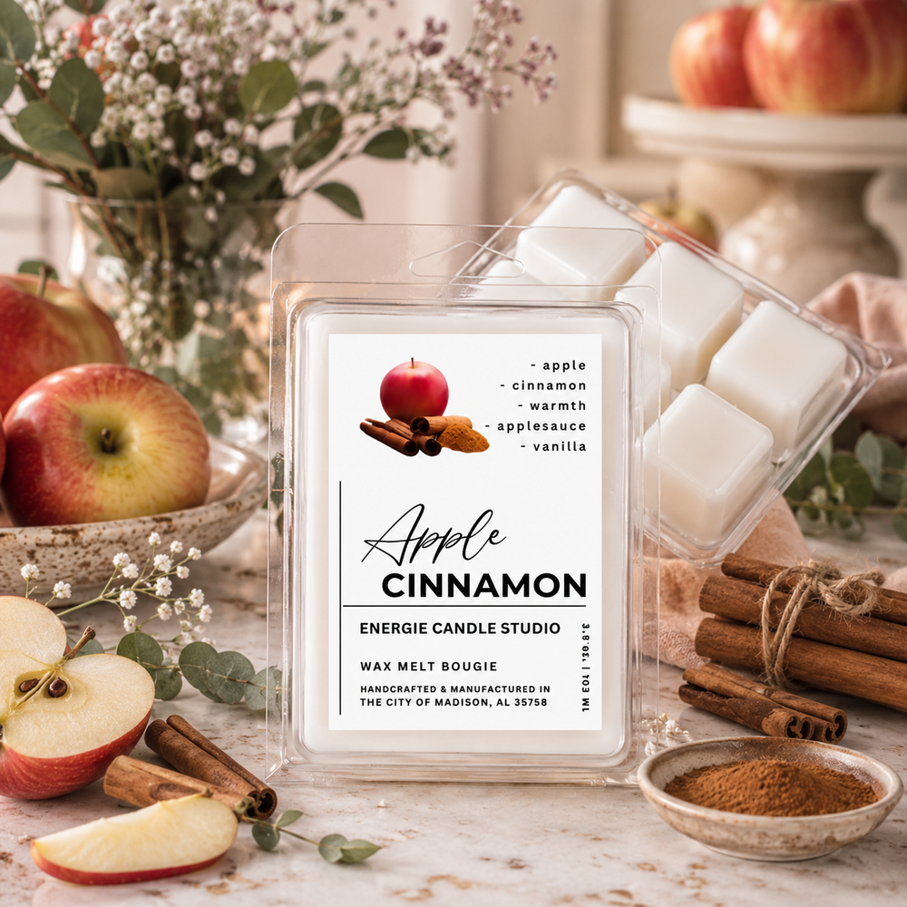 A clear plastic clamshell package of Energize Candle Studio 'Apple Cinnamon' wax melt bougies, displayed on a rustic marble surface surrounded by apples, cinnamon sticks, and flowers.