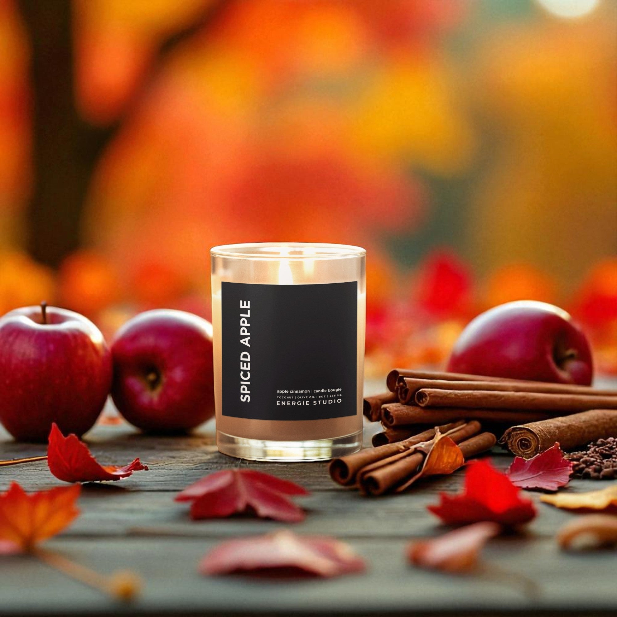 Spiced Apple candle with apples and cinnamon sticks on a wooden surface with a blurred autumn background.