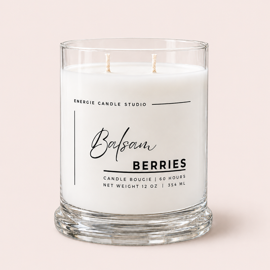 A two-wick scented candle in a clear glass jar with white wax, labeled 'Balsam BERRIES' by Energie Candle Studio, set against a solid pale pink background.