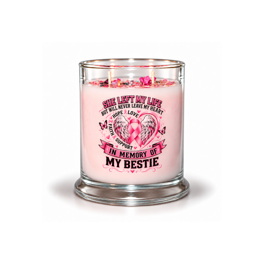 A pink scented candle in a clear glass jar with a glass base, lit with three wicks. The front of the jar features a graphic with a pink ribbon heart, wings, and the text 'SHE LEFT MY LIFE BUT WILL NEVER LEAVE MY HEART.
