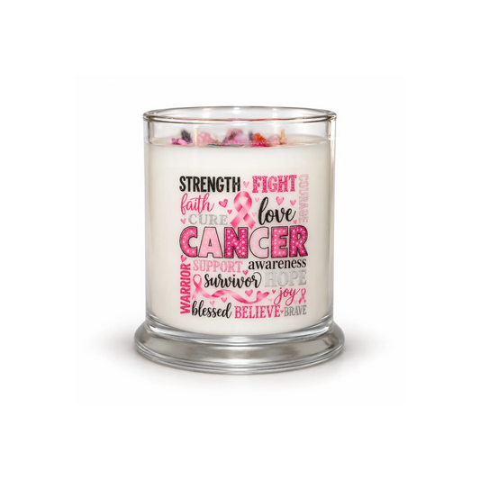 A glass jar candle with white wax and a clear glass base, featuring a printed front design with pink and black text celebrating cancer awareness and support words like strength, faith, love, courage, and belief. The candle is shown lit on a clean white background.