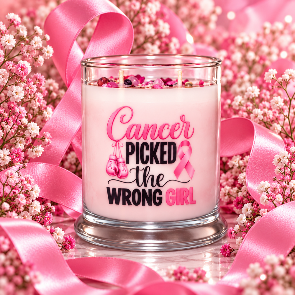 A pink wax candle in a clear glass jar with the printed message 'Cancer Picked the Wrong Girl' and a pink ribbon graphic, surrounded by pink satin ribbons and white baby's breath flowers.
