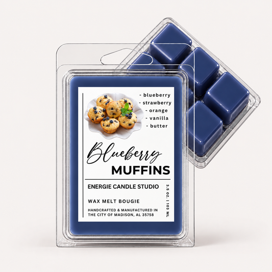 Two clear plastic wax melt clamshells on a light warm-gray background. The front package contains a deep blue wax melt labeled 'Blueberry Muffins' with a cookie photo and scent notes; a second clamshell sits behind it showing additional blue wax melts inside.