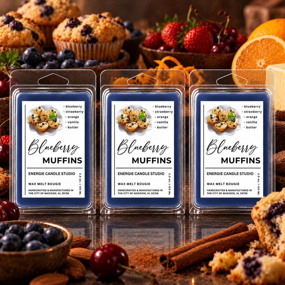 Three packaged wax melts labeled Blueberry Muffins arranged on a reflective surface, with muffins, berries, oranges, and cinnamon sticks used as styled props in a warm kitchen-like setting.