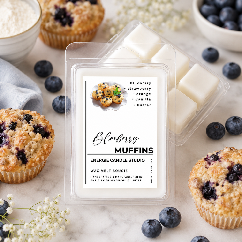 A wax melt package labeled 'Blueberry Muffins' by Energie Candle Studio, shown in a styled flat-lay with blueberries, muffins, and small flowers on a marble surface.