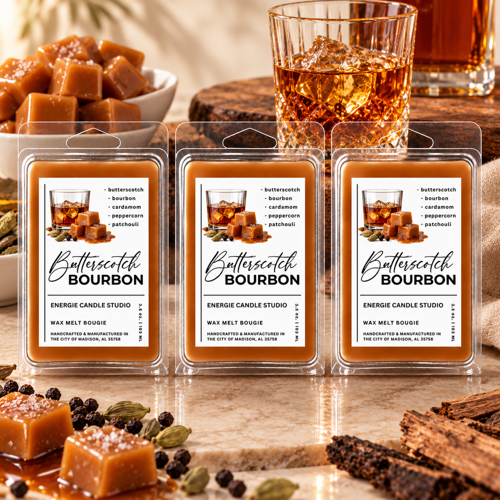 Three packaged wax melts labeled 'Butterscotch Bourbon' by Energie Candle Studio are arranged on a marble surface with caramel cubes, a glass of bourbon, and spices in the background.