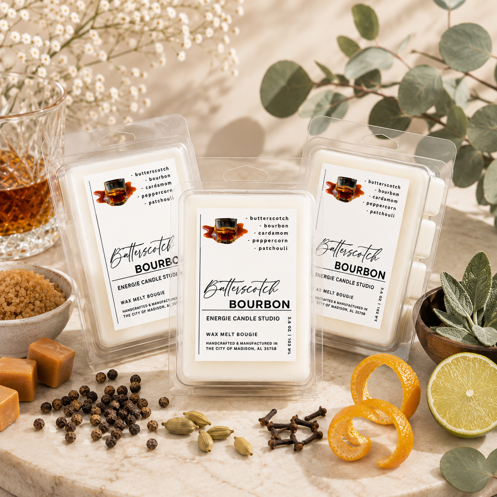 Three clear plastic wax melt packages labeled 'Bathscatch Bourbon' are arranged on a marble surface with decorative ingredients including peppercorns, cloves, orange slices, a lime, brown sugar, and eucalyptus leaves. The scene is styled in a warm, natural setting with no people or animals.