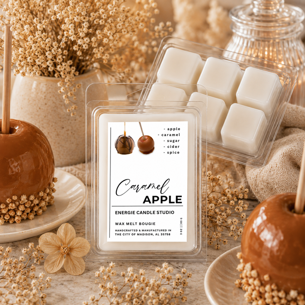 A wax melt package labeled 'Caramel Apple' by Energie Candle Studio is centered in a styled tabletop scene with caramel-apple decorations, dried flowers, and a second open wax melt tray behind it.