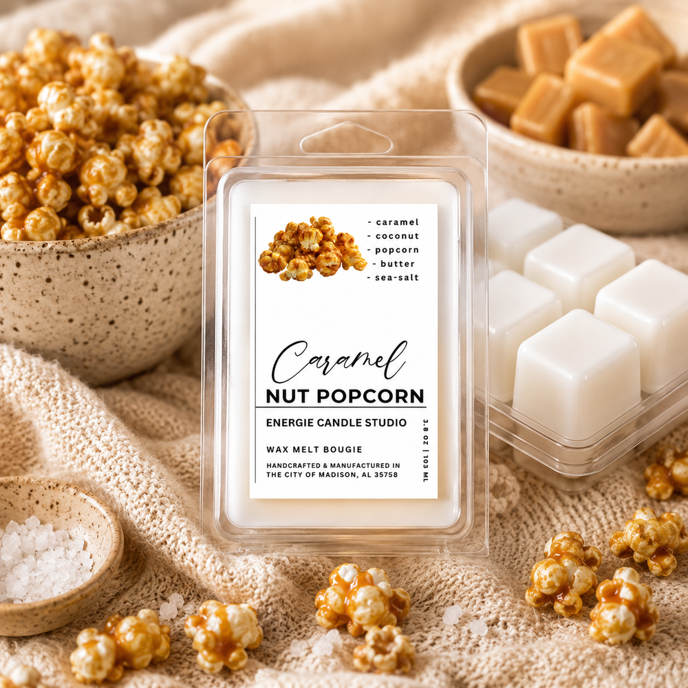 A clear plastic clamshell package of wax melts labeled 'Caramel Nut Popcorn' by Energie Candle Studio, surrounded by caramel popcorn, caramel cubes, and white wax cubes on a beige textured fabric background.
