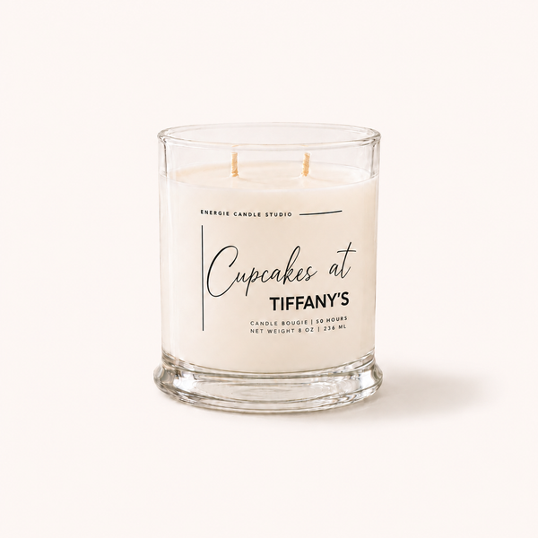 A double-wick candle in a clear glass jar with white wax, featuring a printed label that reads 'ENERGIC CANDLE STUDIO Cupcakes at TIFFANY'S' on a clean, light beige background.