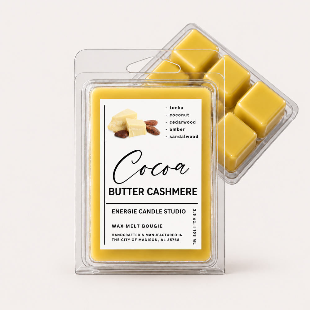Two clear plastic clamshell packages of wax melt are shown on a light warm gray background. The front package is labeled 'Cocoa Butter Cashmere' by Energie Candle Studio, and the rear package shows several yellow wax cubes inside.