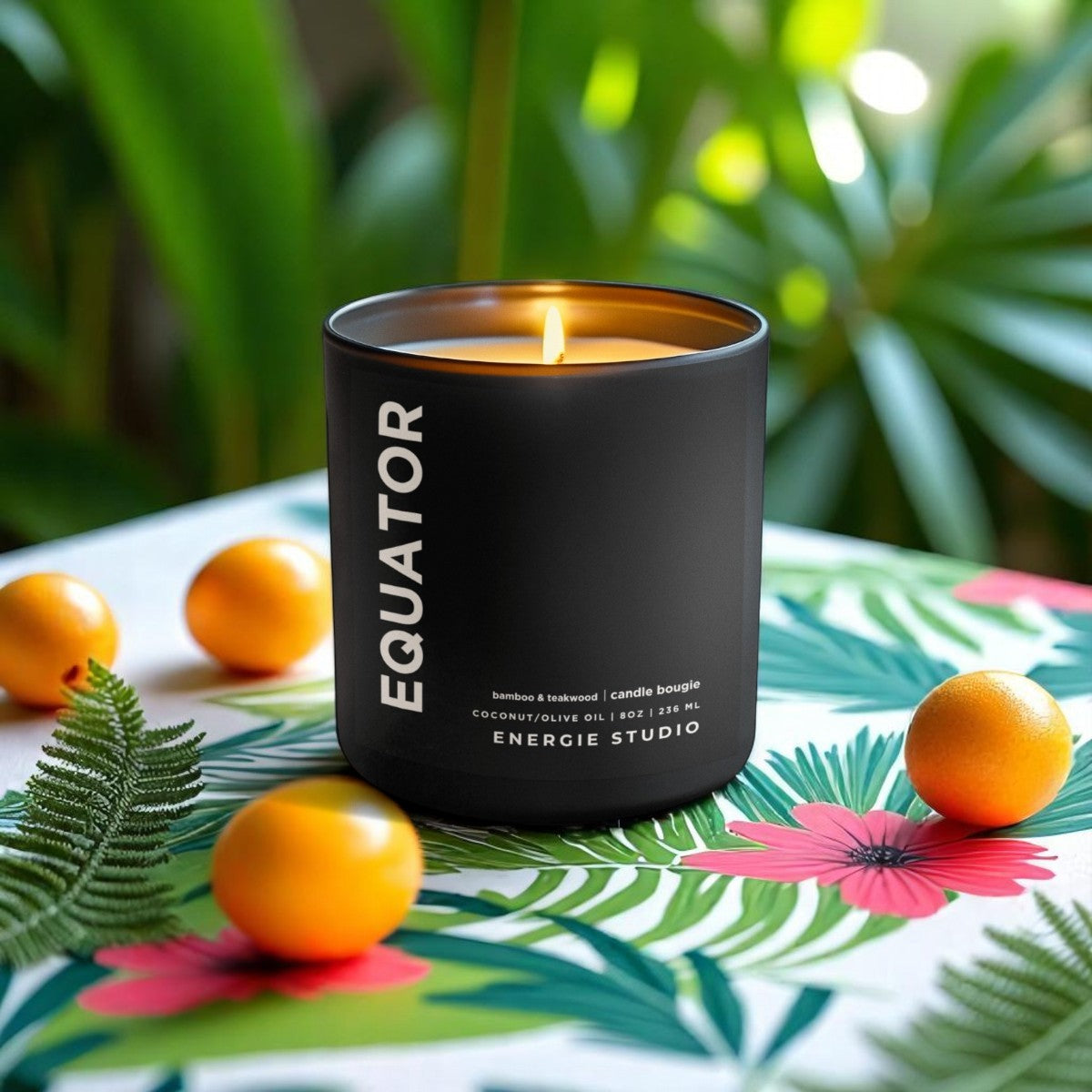 A black candle set on a table with a jungle pattern and yellow tomatoes with green bushes in the background