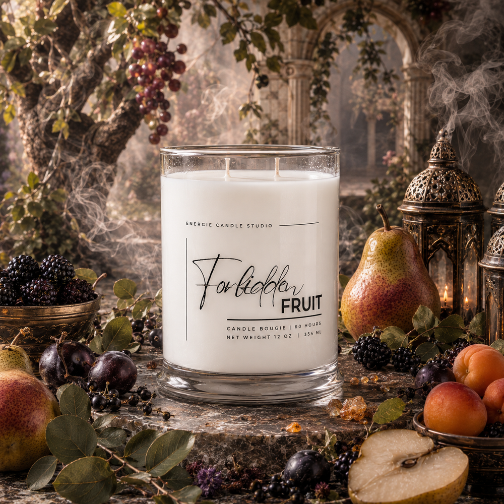 A white scented candle in a clear glass jar labeled 'Forbible Fruit' by Energie Candle Studio, styled in a rustic outdoor garden setting with pears, plums, apricots, lanterns, and steam.