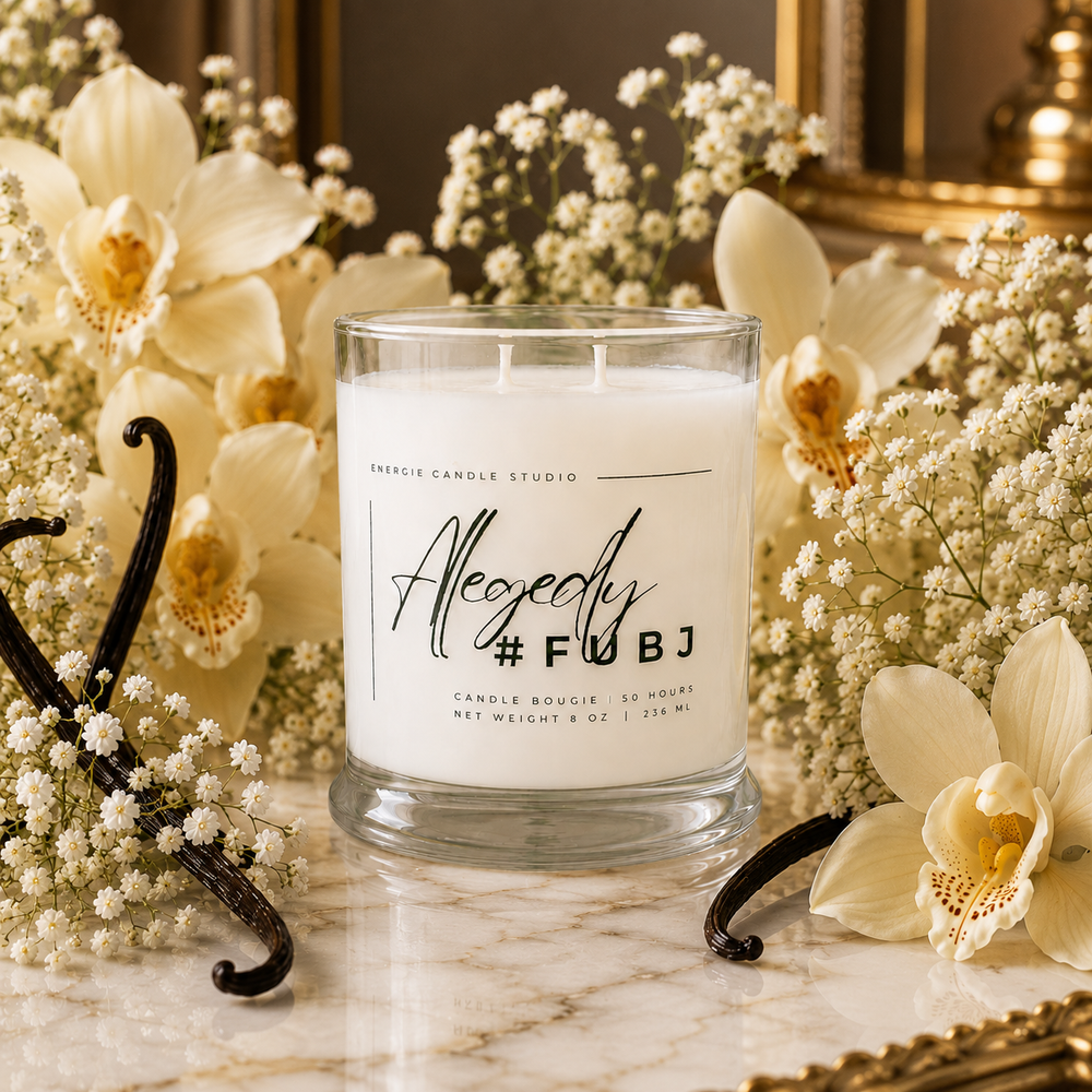 Candle with 'Alegedly #FUBJ' text surrounded by flowers and vanilla beans on a marble surface.