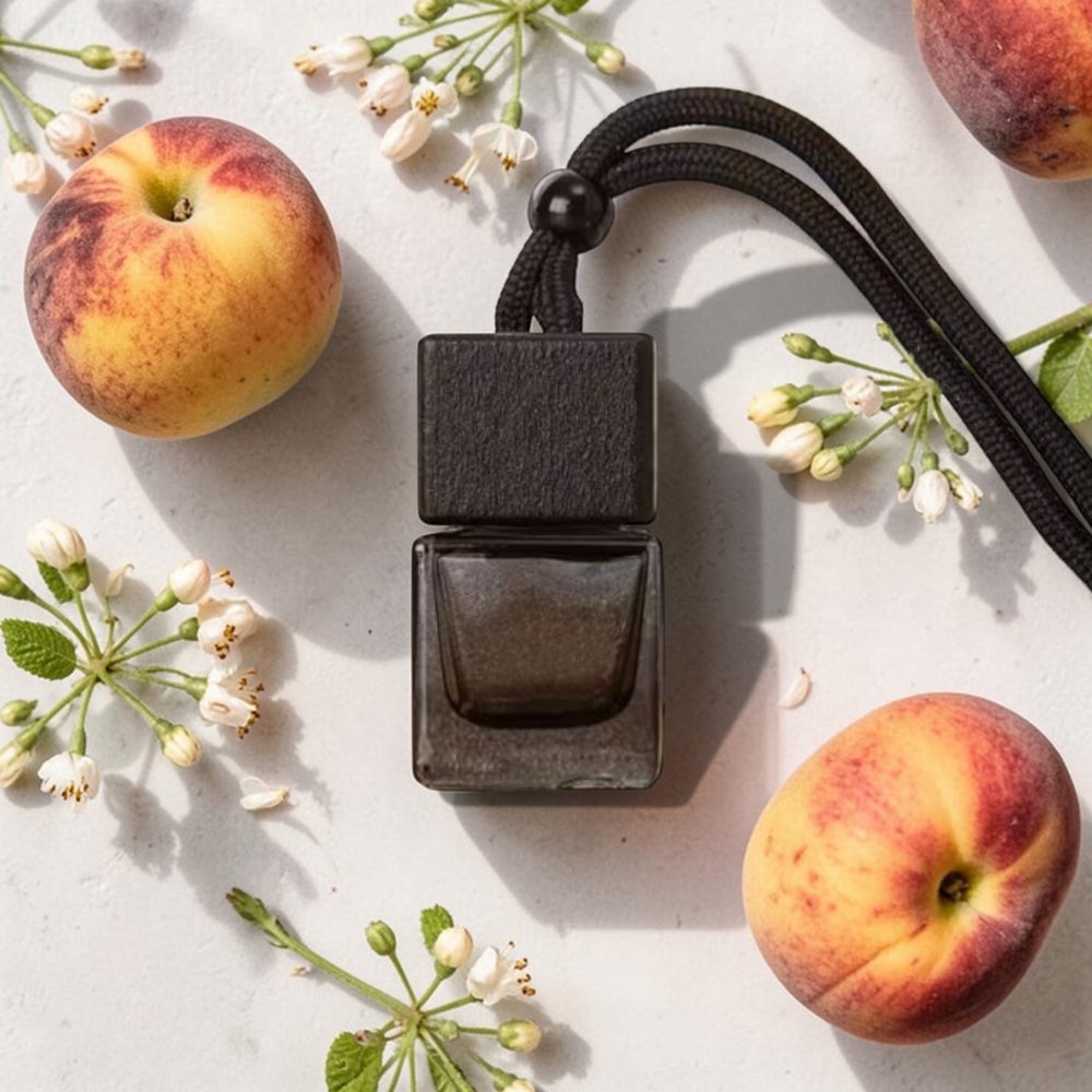 Black rectangular pendant with a cord, surrounded by peaches and flowers on a light surface