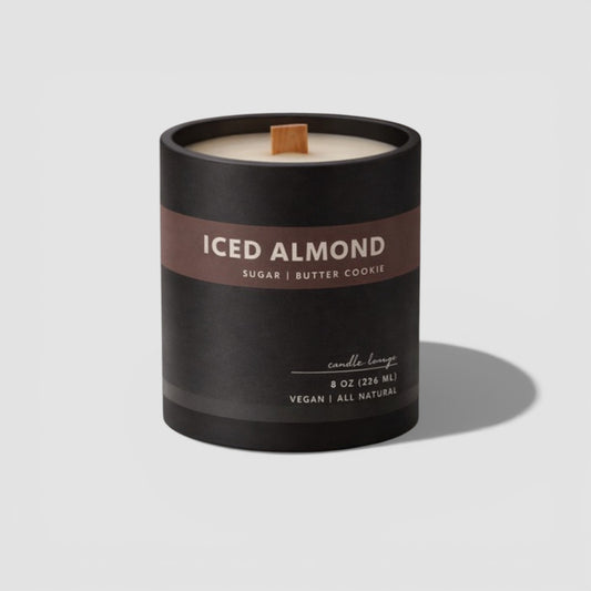Candle labeled 'ICED ALMOND' with a wooden wick on a light gray background