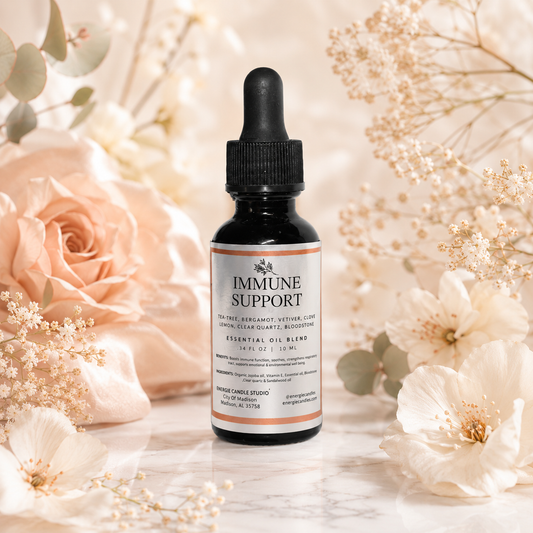A small amber glass dropper bottle labeled 'Immune Support' stands centered on a light marble surface, surrounded by soft cream flowers and botanicals in a warm, styled setting.